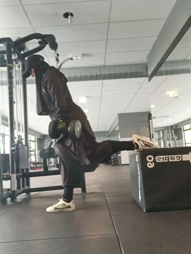 coach-muslima-fit-coach-sportive-en ligne Coach Muslima Fit effectuant un exercice de musculation sur un appareil en salle de sport.